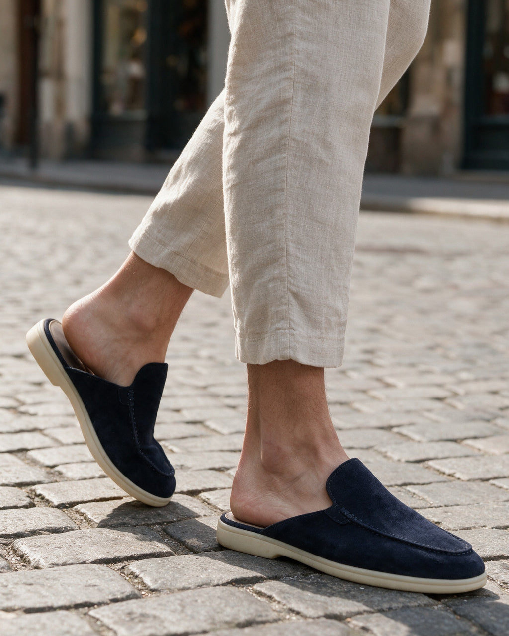 Navy suede slippers worn on a cobbled street with linen trousers