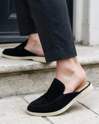Black suede slippers worn with tailored trousers