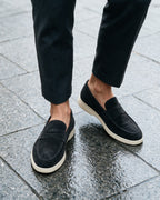 Lorvano Suede Penny Loafers in black suede with cream sole worn on wet granite paving